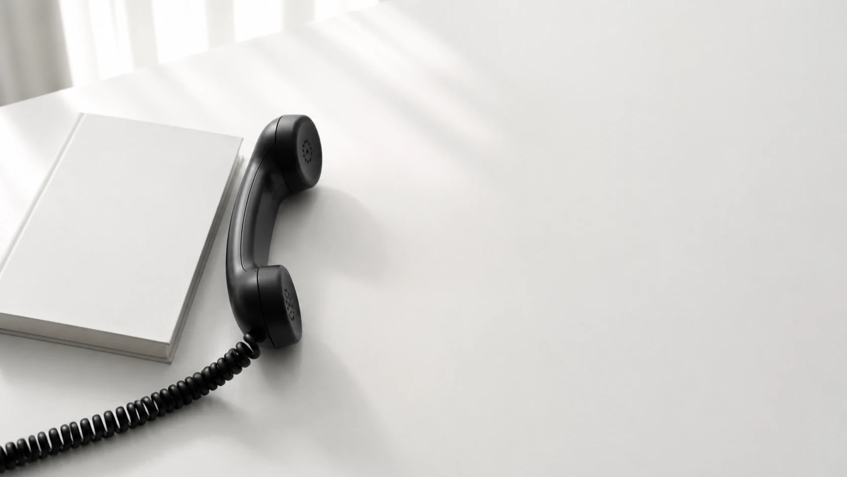 A telephone handset resting beside a closed notebook on a white desk