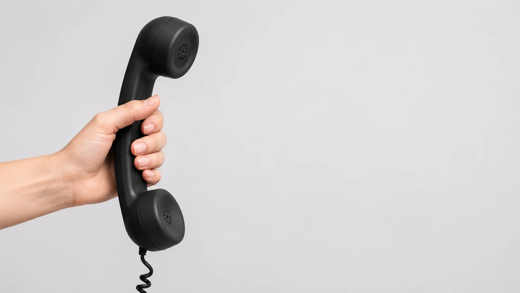 A hand lifting a telephone handset against a plain studio background
